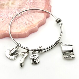 May include: Silver charm bracelet with five charms: a coffee cup, a high heel shoe, a rotary phone, a laptop, and a silver bangle.