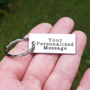 May include: A silver keychain with a silver ring and a rectangular tag that says "Your Personalized Message".