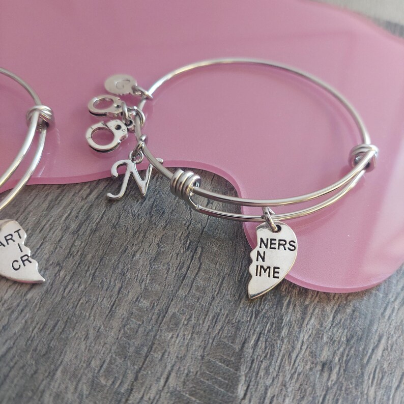 May include: Two silver charm bracelets with a heart charm that says "Partners in Crime" and a charm with a letter "N".