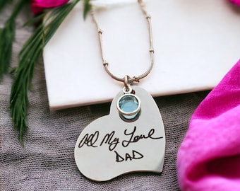May include: Silver heart-shaped pendant necklace with a blue gemstone. The pendant has the handwritten message "All My Love Dad" inscribed on it.