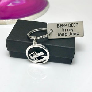 May include: Silver Jeep keychain with a round charm featuring a Jeep driving on a dirt road. The keychain also includes a rectangular tag with the text "Beep Beep in my Jeep Jeep".