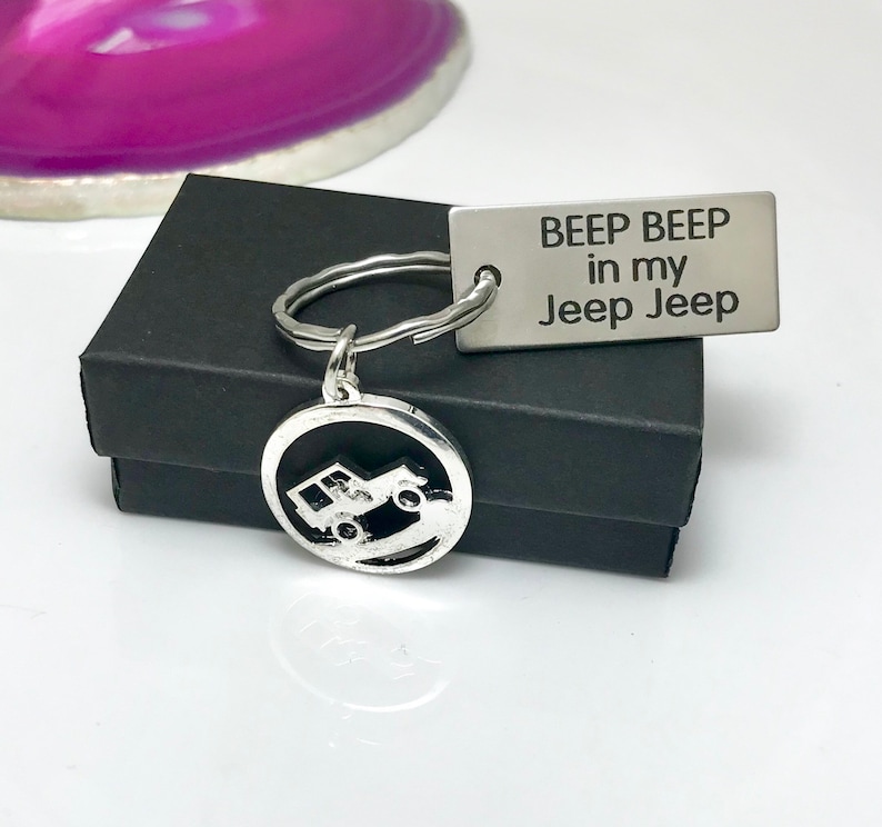 May include: Silver Jeep keychain with a round charm featuring a Jeep driving on a dirt road. The keychain also includes a rectangular tag with the text "Beep Beep in my Jeep Jeep".