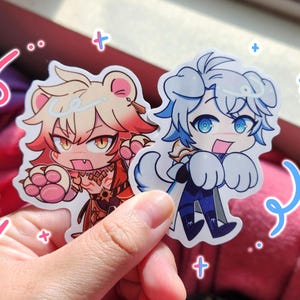 May include: Two die-cut vinyl stickers featuring anime-style characters. One sticker depicts a character with bear ears, orange hair, and red clothing. The second sticker shows a character with blue hair, dog ears, and a blue outfit with white paws.