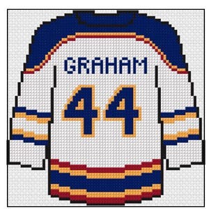 Könnte beinhalten: Kreuzstichmuster eines Hockey-Trikots. Das weiße Trikot hat blaue, goldene und rote Akzente. Der Name "GRAHAM" ist über den Schultern gestickt, die Nummer "44" auf dem Rücken.