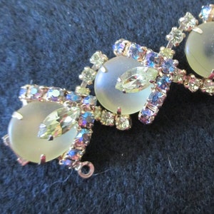 May include: Vintage jewelry piece featuring three large, frosted, oval-shaped stones. The stones are surrounded by smaller, iridescent, and clear crystals in a gold-toned setting. The design includes leaf-shaped accents.