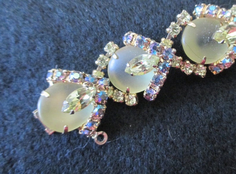 May include: Vintage jewelry piece featuring three large, frosted, oval-shaped stones. The stones are surrounded by smaller, iridescent, and clear crystals in a gold-toned setting. The design includes leaf-shaped accents.