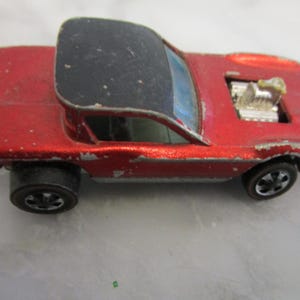 May include: A red toy car with a black roof and a silver engine. The car has black wheels and a silver body.
