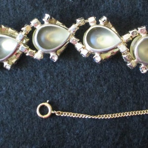May include: A vintage gold-toned bracelet featuring pear-shaped, iridescent stones. Each stone is framed by a gold setting and surrounded by small, clear rhinestones. The bracelet has a safety chain and a clasp closure.