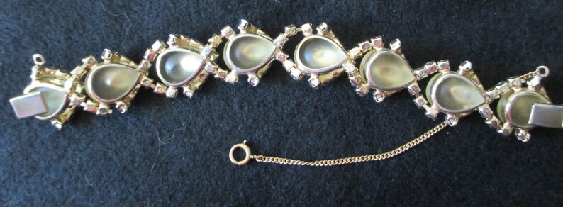 May include: A vintage gold-toned bracelet featuring pear-shaped, iridescent stones. Each stone is framed by a gold setting and surrounded by small, clear rhinestones. The bracelet has a safety chain and a clasp closure.