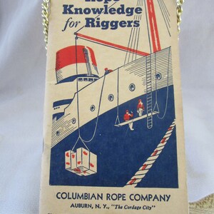 May include: A vintage booklet titled Rope Knowledge for Riggers by the Columbian Rope Company of Auburn, N.Y. The cover features a blue and red graphic illustration of a ship with crew members and cargo, suspended by a gold-colored metal chain.
