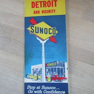 May include: A vintage Sunoco gas station map of Detroit and vicinity from 1962-1963. The map features a blue background with a yellow Sunoco logo and red arrows. The map also includes a small illustration of a Sunoco gas station with two cars being filled with gas.