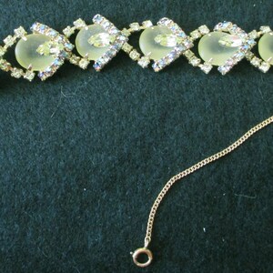 May include: A vintage bracelet featuring heart-shaped, pale yellow stones set in a diamond-shaped pattern. Each heart is surrounded by clear, iridescent rhinestones. A delicate gold chain extends from the clasp.