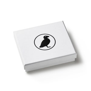 May include: A white square box with a black bird logo inside a circle. The box is closed and has a simple, clean design. The bird is a silhouette, and the overall aesthetic is minimalist.