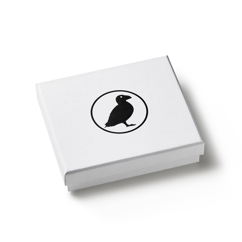 May include: A white square box with a black bird logo inside a circle. The box is closed and has a simple, clean design. The bird is a silhouette, and the overall aesthetic is minimalist.