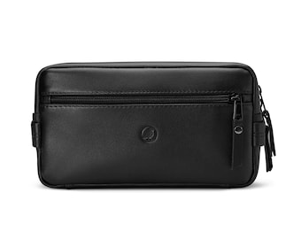 May include: Black rectangular travel bag with a zipper closure and a small logo. The bag has a wrist strap and a textured surface. The bag is made of a leather-like material.