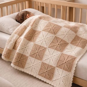 May include: A cream and tan crochet baby blanket with a geometric pattern. The blanket is draped over a baby in a wooden crib. The blanket's design features alternating squares of cream and tan, with a scalloped edge.