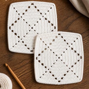May include: Two square white crochet coasters featuring a central diamond pattern created with openwork stitches. The coasters are made from fine white yarn and exhibit a consistent, tight stitch construction throughout the square shape.