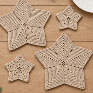 Puede incluir: Cuatro posavasos de ganchillo en forma de estrella de varios tamaños, hechos de hilo beige claro. El diseño presenta un patrón de puntos denso y texturizado que irradia desde el centro de cada estrella, creando un aspecto geométrico uniforme.