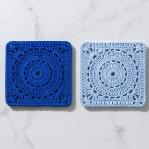 Könnte beinhalten: Zwei quadratische Häkeluntersetzer, einer in tiefem Königsblau und der andere in hellem Himmelblau. Jeder Untersetzer zeigt ein kreisförmiges, von Mandalas inspiriertes Muster mit komplexen Stichen, die von der Mitte zu den Ecken strahlen.
