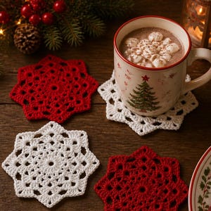 May include: A set of four star-shaped crochet coasters in solid red and white colors. The coasters feature an intricate, openwork lace pattern. One white coaster supports a ceramic mug filled with hot cocoa and marshmallows, decorated with a tree.