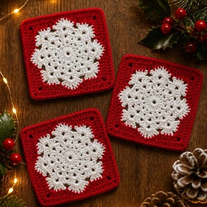 May include: Three square crochet coasters featuring a white snowflake pattern centred on a solid red background. Each coaster is crafted with intricate white yarn stitches forming a star-like snowflake design surrounded by a red square border.