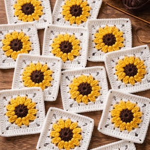 May include: A collection of handmade crochet squares featuring a sunflower design. Each square has a white border with a yellow and brown sunflower in the center. Yarn and a crochet hook are visible in the background.