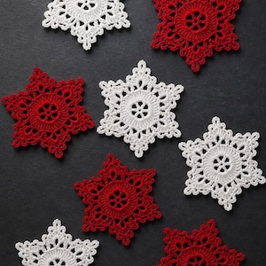 May include: A collection of seven crocheted snowflake ornaments arranged in a scattered pattern. Four snowflakes are bright white and three are deep red. Each piece features a circular center with a six-pointed star design and intricate lace edges.