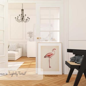 a bright and airy living room with a large window, a chandelier, a white sofa, a black chair, and a framed illustration of a pink flamingo.