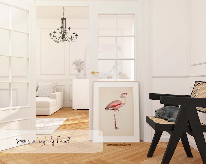 a bright and airy living room with a large window, a chandelier, a white sofa, a black chair, and a framed illustration of a pink flamingo.