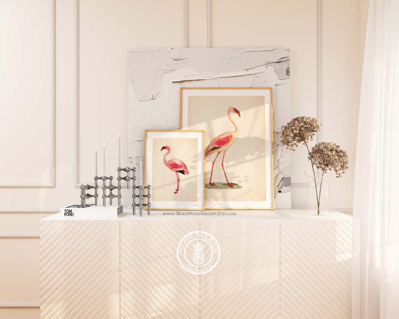 May include: Two framed prints of pink flamingos on a white background, with a silver metal candle holder and a book on a white chevron patterned dresser. The text on the bottom of the print reads "www.BeachHouseGallery.Etsy.com".