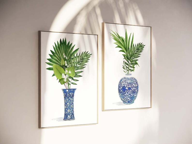 K&ouml;nnte beinhalten: Zwei gerahmte Drucke von Aquarellgem&auml;lden mit blauen und wei&szlig;en Porzellanvasen mit gr&uuml;nen, bl&auml;ttrigen Pflanzen. Die Vasen haben komplizierte Blumenmuster.