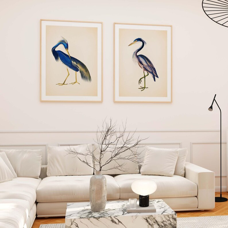 a living room with a white sofa, a marble coffee table, and two framed paintings of blue herons hanging on the wall above the sofa.