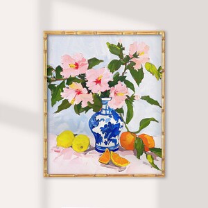 May include: A painting of a blue and white porcelain vase filled with pink hibiscus flowers. The vase is sitting on a pink surface with lemons and oranges around it.