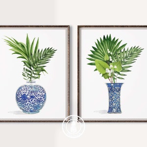 K&ouml;nnte beinhalten: Zwei gerahmte Drucke von blauen und wei&szlig;en Porzellanvasen mit gr&uuml;nen, bl&auml;ttrigen Pflanzen. Die Vasen sind mit floralen Mustern verziert.
