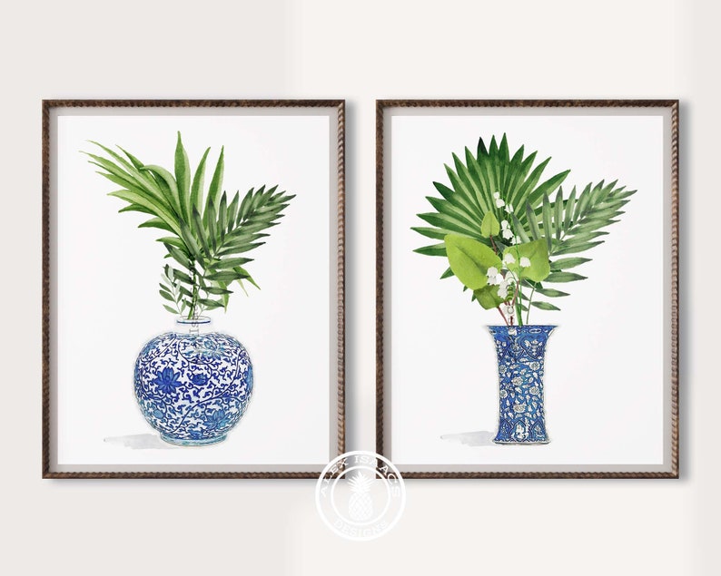 K&ouml;nnte beinhalten: Zwei gerahmte Drucke von blauen und wei&szlig;en Porzellanvasen mit gr&uuml;nen, bl&auml;ttrigen Pflanzen. Die Vasen sind mit floralen Mustern verziert.