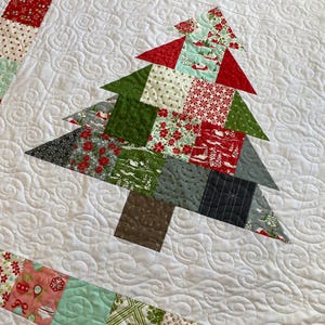 May include: A white quilt with a patchwork Christmas tree design. The tree is made of red, green, and gray fabric squares. The quilt is quilted with a swirling pattern.