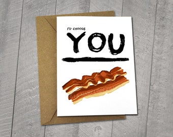 May include: A white card with black text that reads "I'd choose YOU" with a line drawn under the word "YOU".  Below the line is a cartoon image of bacon. The card is 5x6.5 inches and comes with a 5x7 inch envelope.