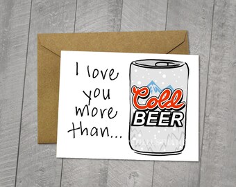 May include: A white card with black text that reads "I love you more than..." and a drawing of a can of beer with the words "Cold Beer" in red and black. The can is on a white background with a snowy mountain scene.