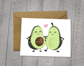 May include: A blank greeting card with an original illustration of two avocado halves with faces and arms. The avocados are holding hands and have a pink heart above them. The card is 5x6.5 inches and comes with a 5x7 inch envelope.
