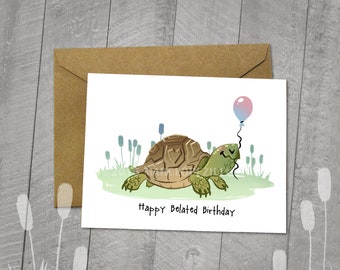 May include: A white greeting card with a cartoon turtle holding a balloon. The card reads "Happy Belated Birthday" in black text. A brown envelope is behind the card. The illustration is on a 5x6.5 inch blank card.