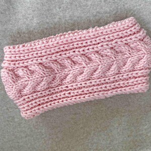Peut inclure: Un bandeau en tricot rose avec un motif en câble.