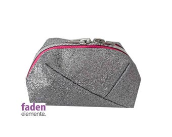 May include: A silver glitter makeup bag with a pink zipper. The bag has a geometric design.