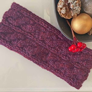 Peut inclure: Un bandeau en tricot violet avec un motif en tricot torsadé. Le bandeau est sur une surface blanche.
