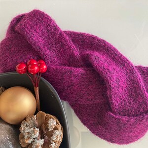 Peut inclure: Un bandeau en tricot violet avec une texture douce et duveteuse. Le bandeau est plié et torsadé, créant un design unique et élégant.