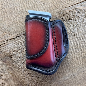 Może przedstawiać: Czerwona skórzana kabura na magazynek z czarnymi szwami i srebrnym magazynkiem w środku.