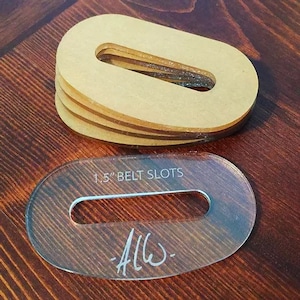 May include: A stack of light brown oval-shaped acrylic templates with a rectangular cutout, and a clear template with the text "1.5" BELT SLOTS" and a signature. The templates are on a dark wood surface.