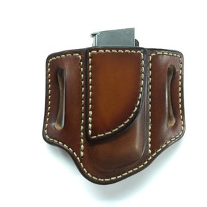 Może przedstawiać: Brązowa skórzana kabura z kieszenią na magazynek. Kabura ma pikowany wzór i jest wykonana z wysokiej jakości skóry.