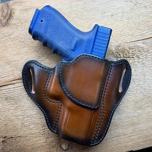 Puede incluir: Una funda de cuero marrón con una pistola azul en su interior. La funda tiene un bucle para el cinturón y está diseñada para llevar oculta.