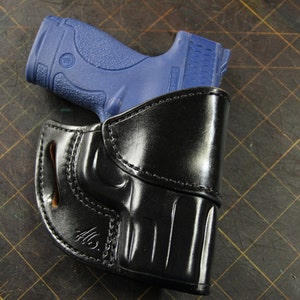 May include: A black leather holster with a blue handgun inside. The holster has a belt loop and a snap closure.