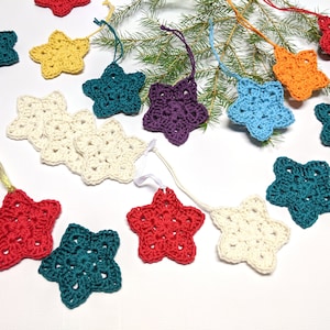 May include: A garland of crocheted star ornaments in various colors, including teal, red, purple, white, and orange. The stars are strung together with white ribbon and are perfect for decorating a Christmas tree or adding a festive touch to any room.